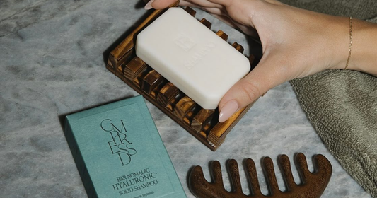 Hand holding a bar of shampoo over a wooden soap dish.