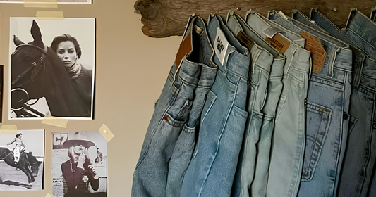 Row of blue jeans hanging on a wooden rack with vintage horse and rider photos on the wall.