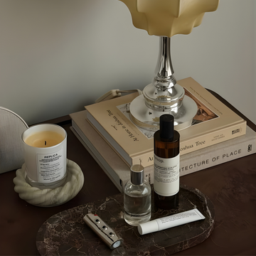 Candle, bottles, and a tube on a marble tray with books in the background